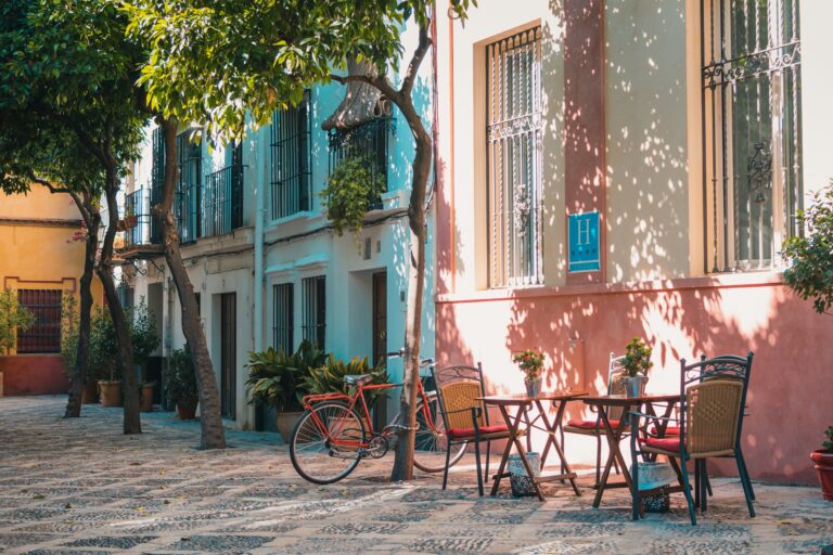 Outdoor café tables and bicycle on a shaded street in Seville, Spain.