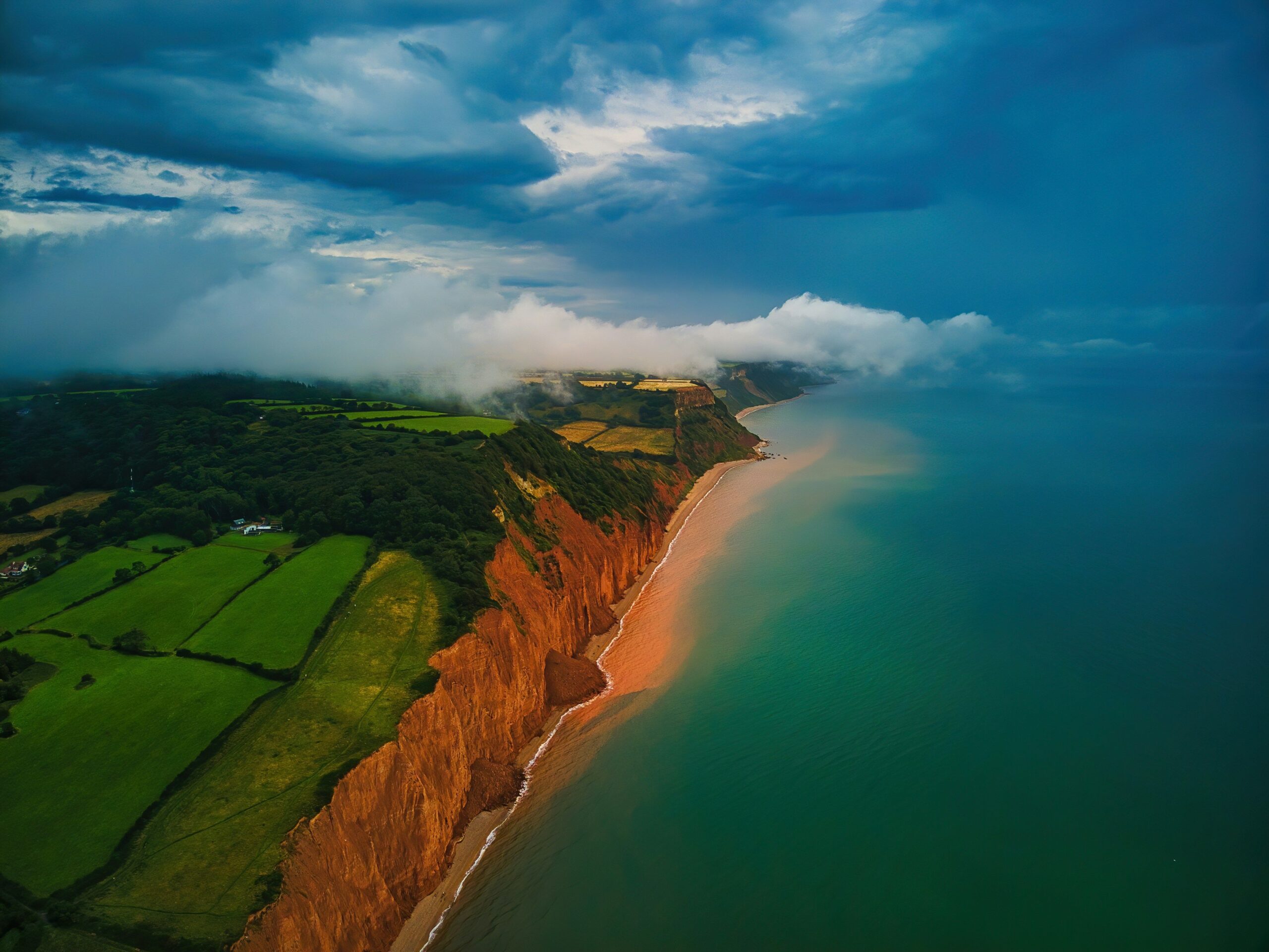 Red sandstone cliffs and farmland along the coastline near Sidmouth in Devon, UK.