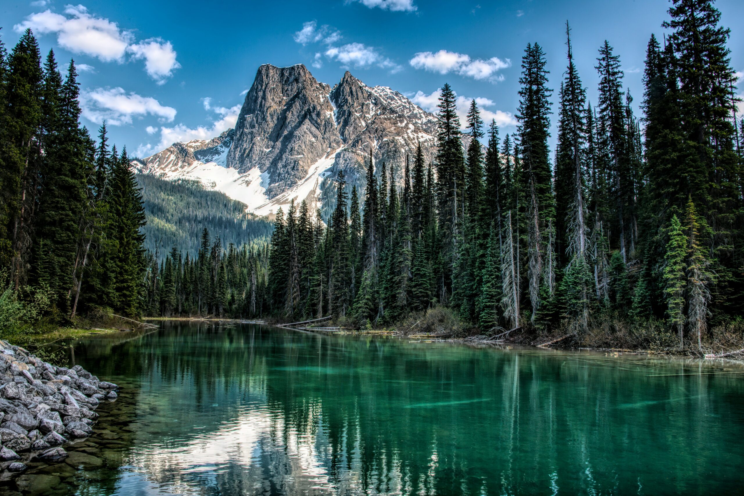 Snow-capped mountain reflected in a clear lake surrounded by pine forest in British Columbia, Canada.