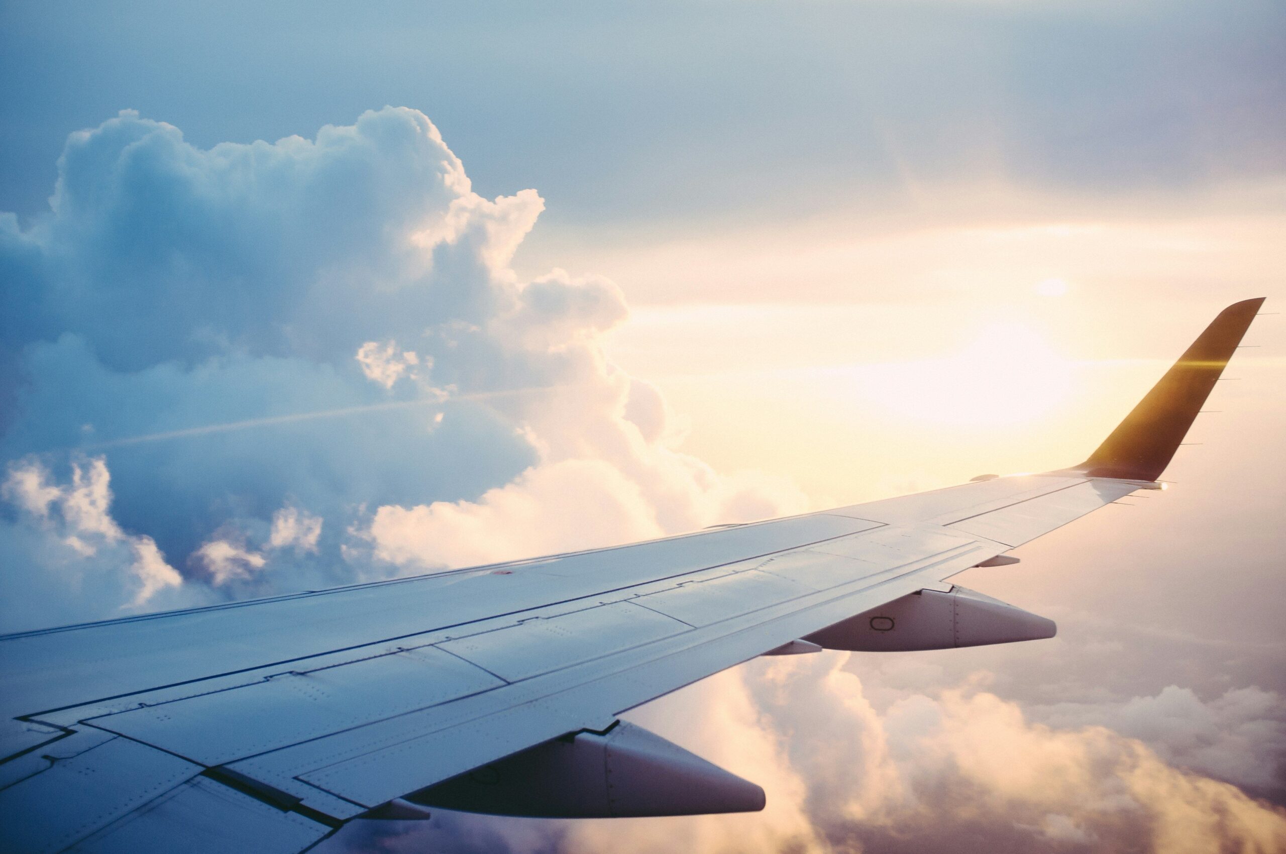 View of an airplane wing above clouds at sunset during a flight.