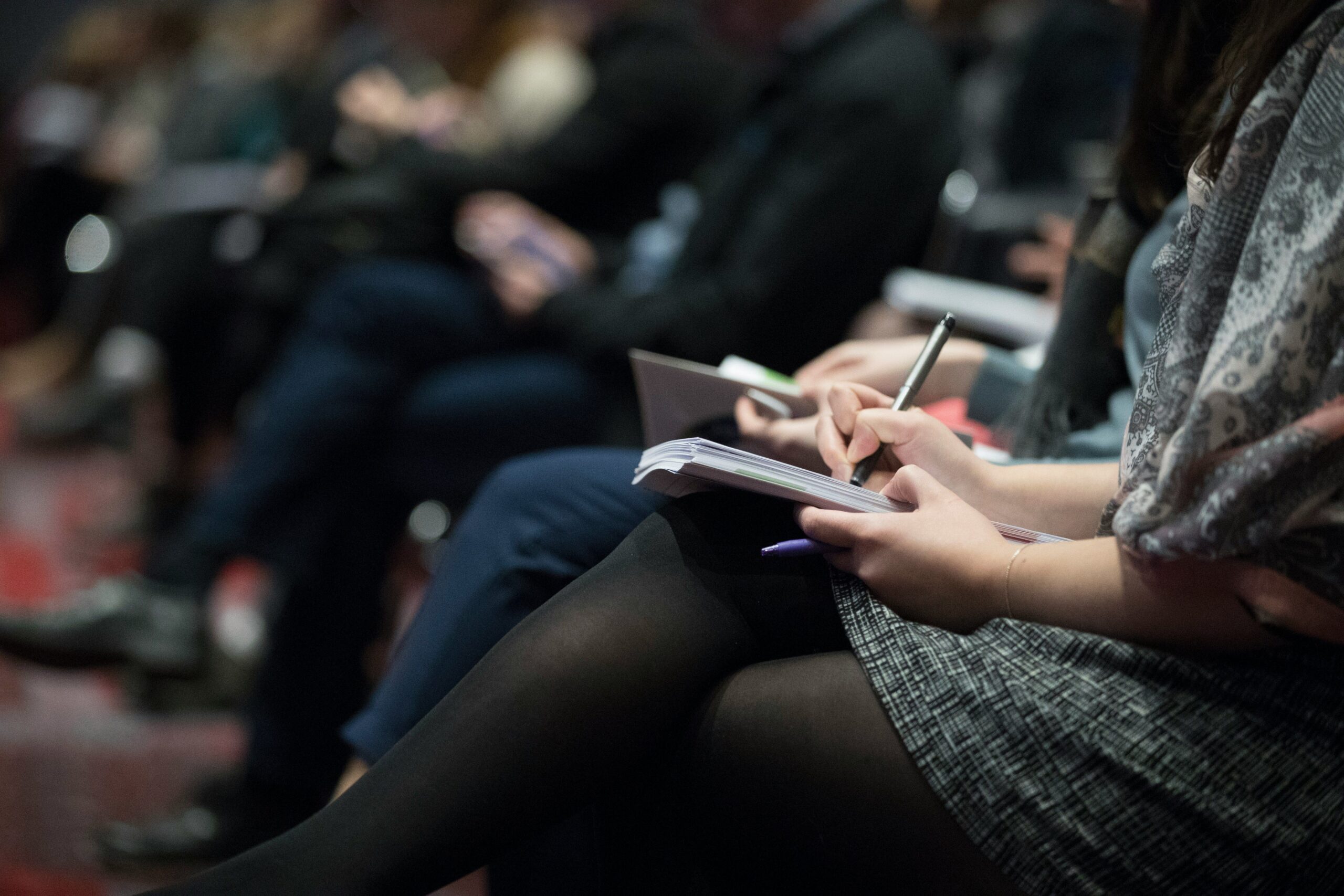 Audience members seated at a conference taking notes in notebooks.