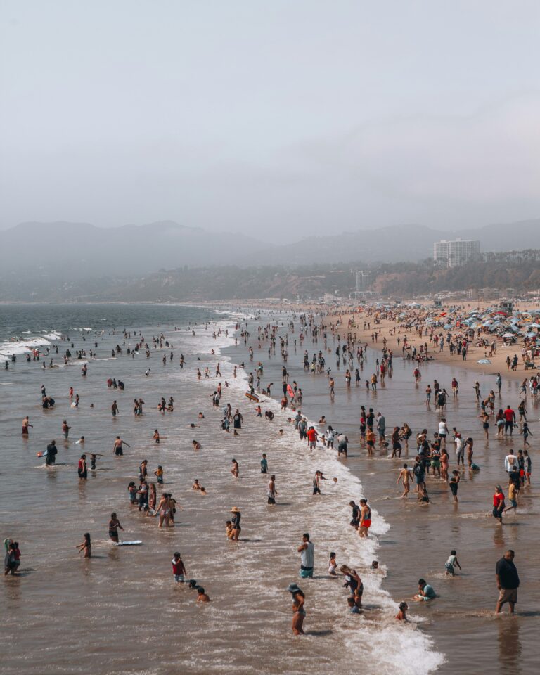 Large crowd of people swimming and walking along a busy beach in California.