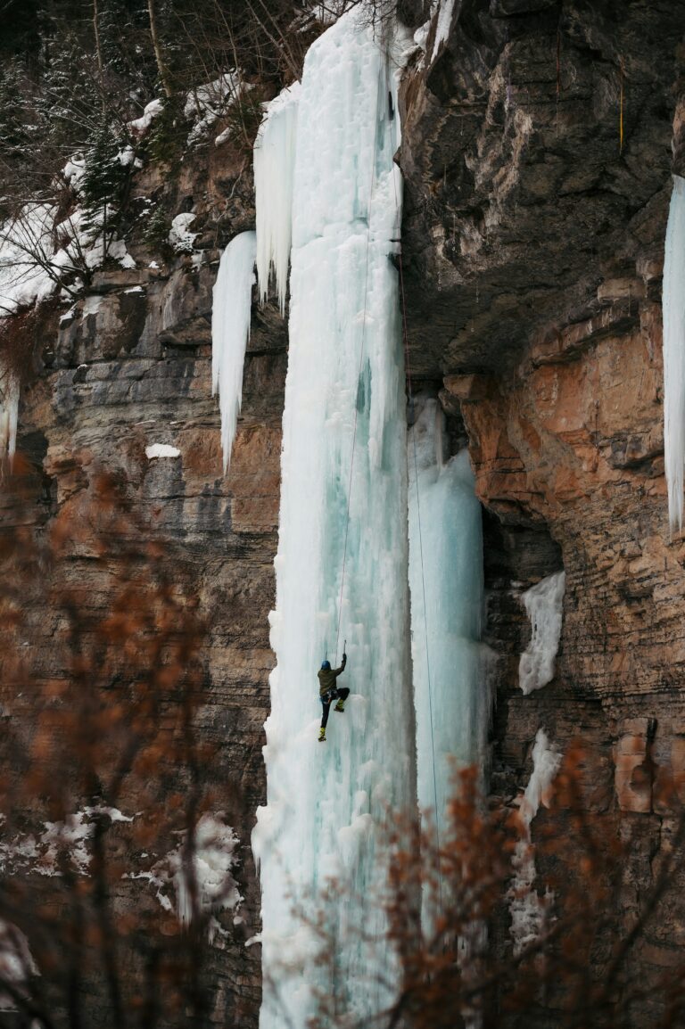 Person ice climbing on a frozen waterfall against a rocky cliff face.