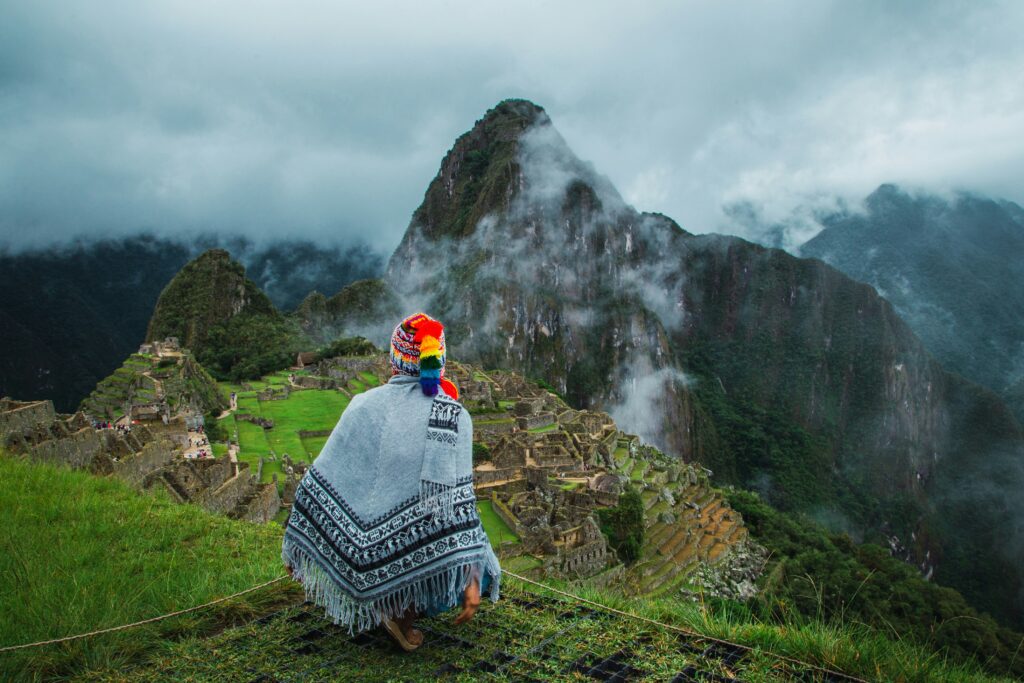 Person wearing a traditional woven shawl overlooking Machu Picchu and mist-covered mountains in Peru.