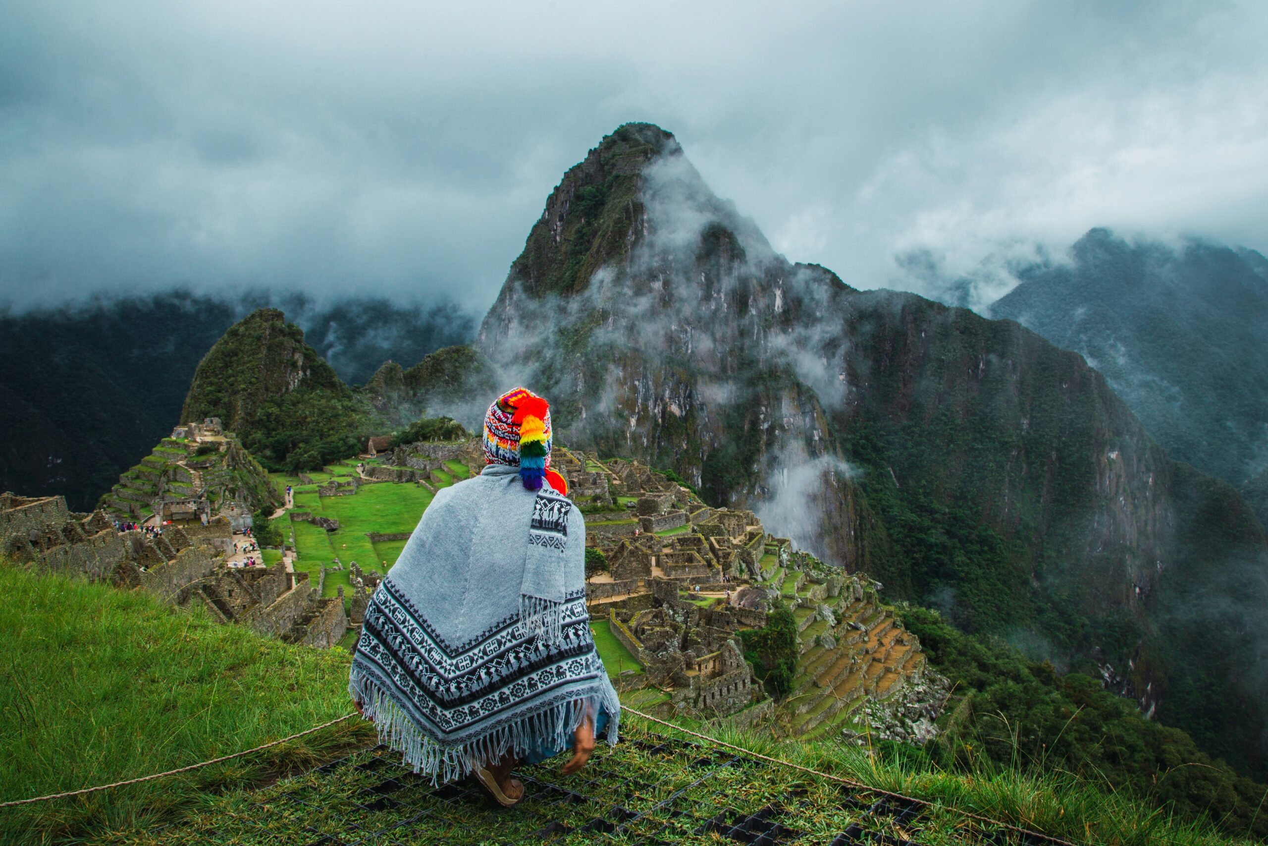 Person wearing a traditional woven shawl overlooking Machu Picchu and mist-covered mountains in Peru.