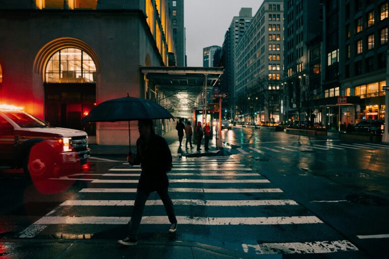 Person holding an umbrella crossing a wet city street at night.