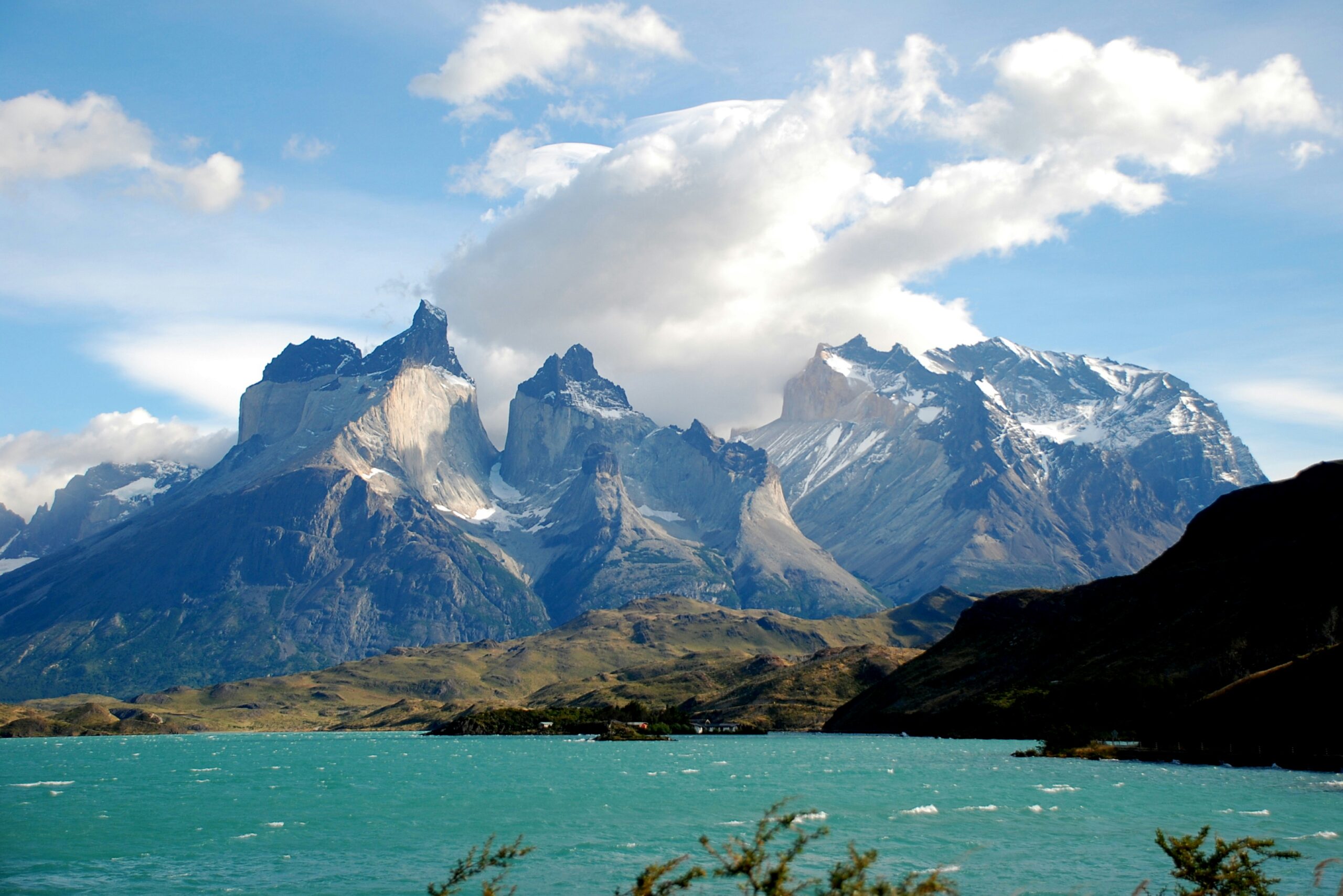 Snow-capped mountain peaks rising above a turquoise lake under a partly cloudy sky.