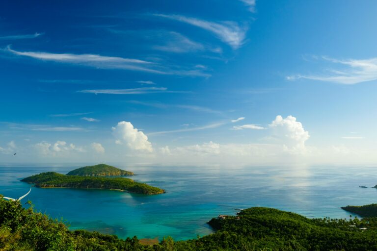 Small green tropical islands surrounded by calm turquoise sea under a blue sky with scattered clouds.