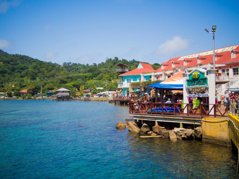 Colourful waterfront restaurants on stilts beside clear blue sea in a tropical coastal town.