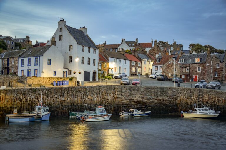 Fishing boats moored at Crail harbour with historic houses behind in Fife, Scotland.
