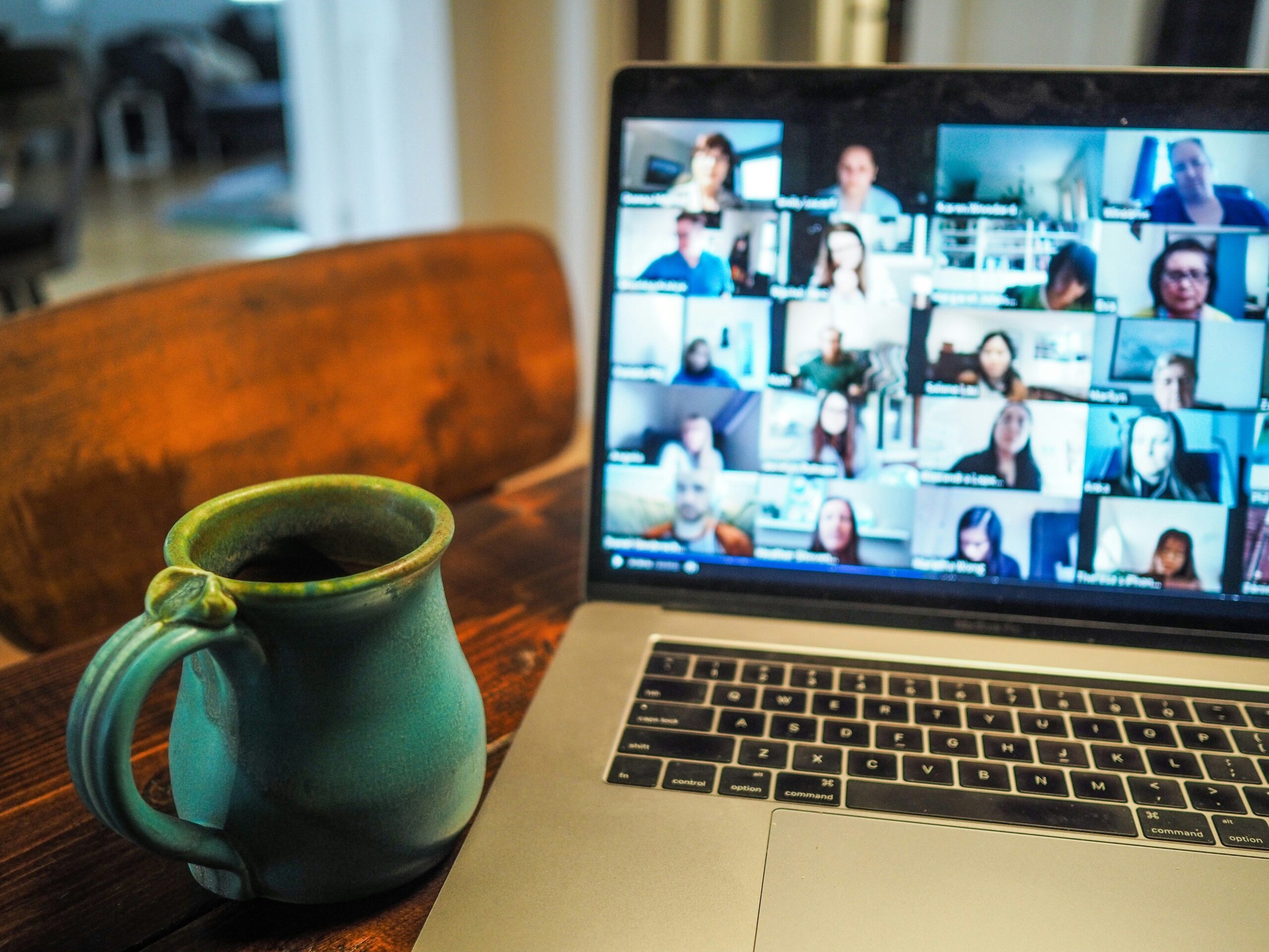 Laptop showing a video call meeting with multiple participants on screen beside a mug on a table.