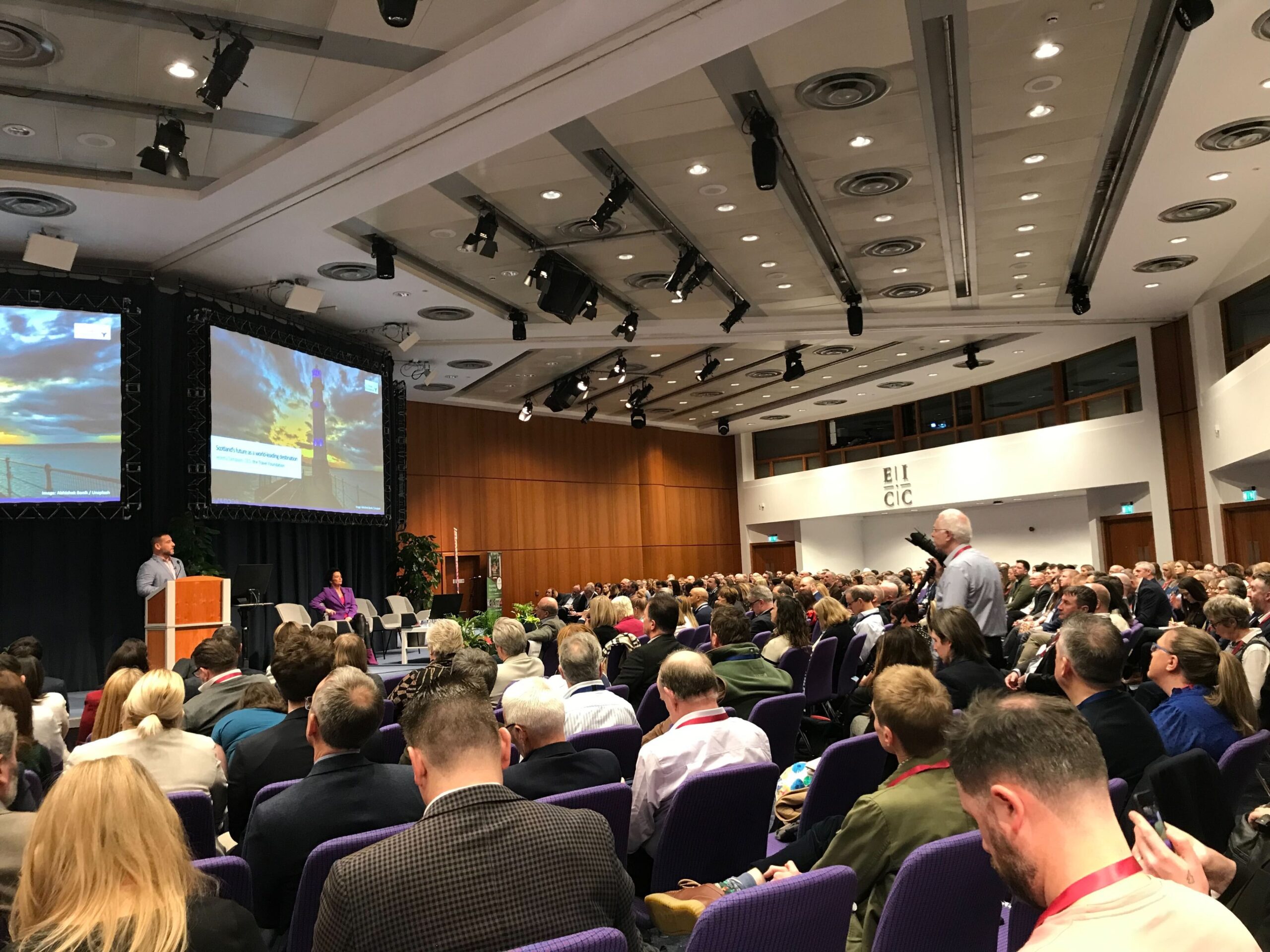 Speaker presenting at a tourism conference keynote session to a large audience in Scotland.