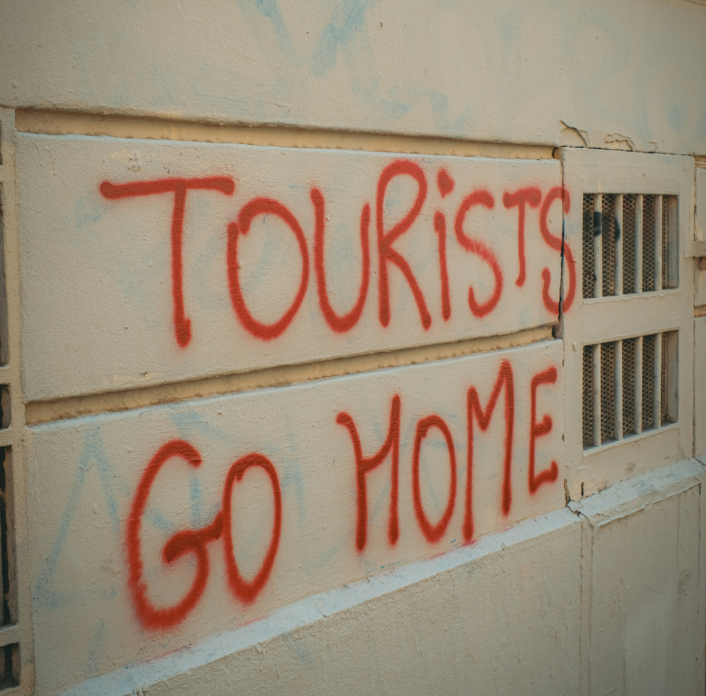 Red graffiti reading “Tourists Go Home” sprayed on the wall of a city building.
