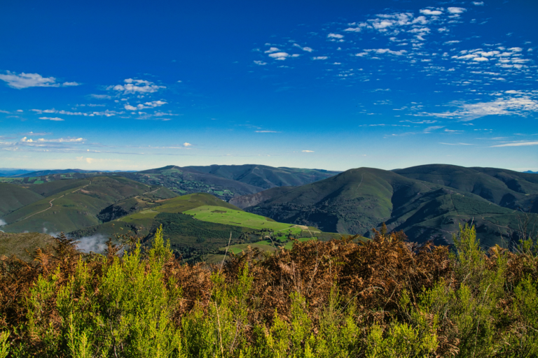 Panoramic view of rolling green mountains and valleys beneath a blue sky with scattered clouds.