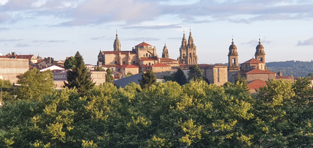 Skyline of Santiago de Compostela with the cathedral rising above trees and historic buildings in evening light.