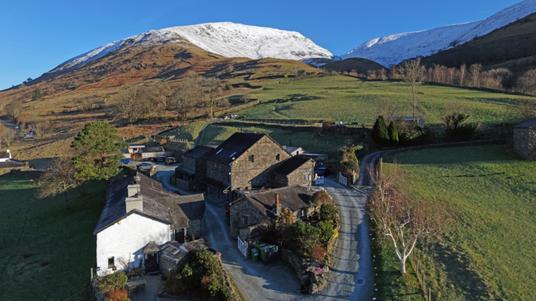 Aerial view of The Yan at Broadrayne in the Lake District, surrounded by farmland and snow-capped fells.